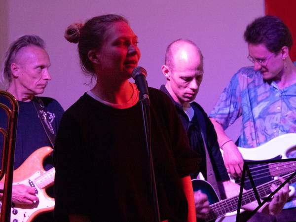 Sängerin vor Mikrofon, 3 Bandmitglieder im Hintergrund